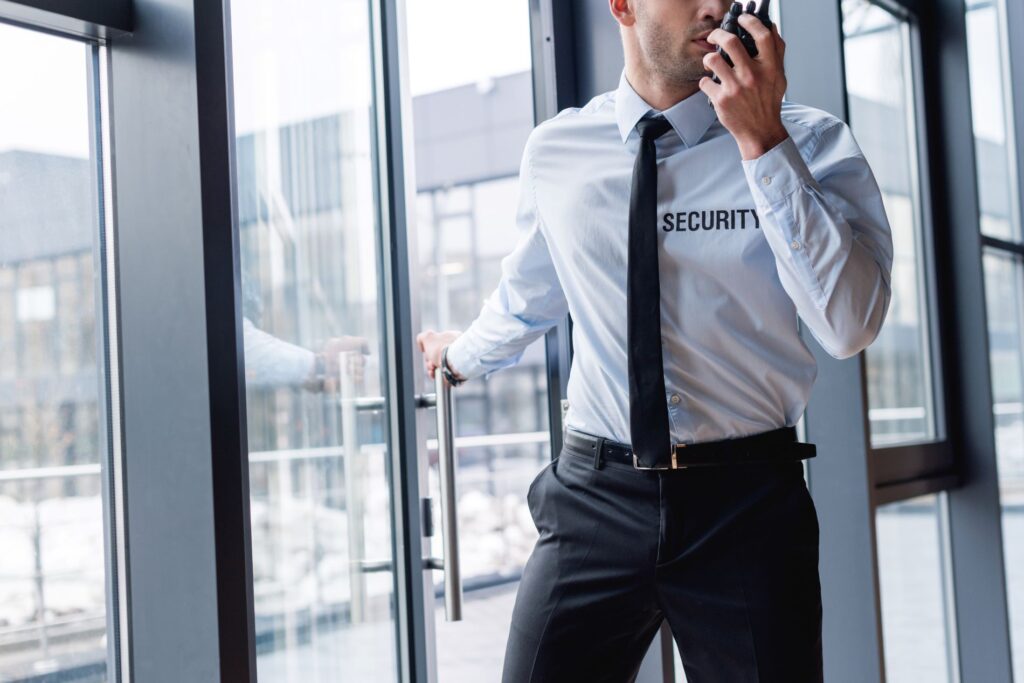 Uniformed security guard entering through a glass door while speaking on a walkie-talkie