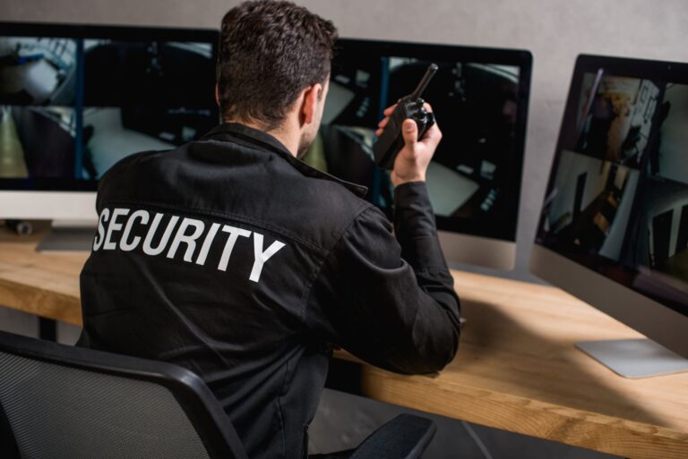 rear view of security guard talking on walkie talkie while monitoring security cameras